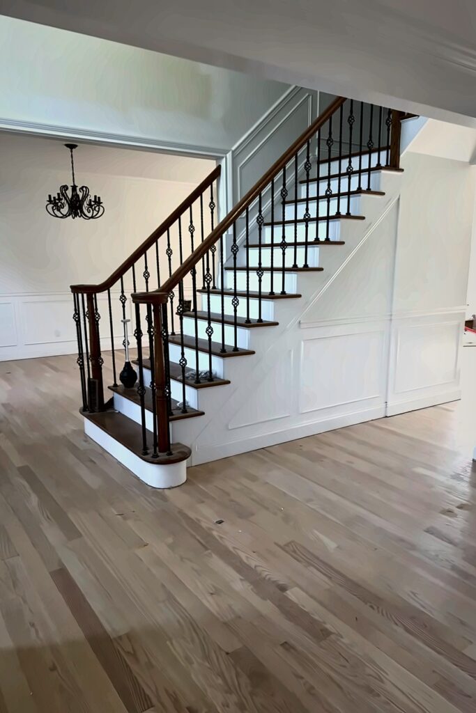 Wood flooring in a foyer beside a white staircase with black metal balusters